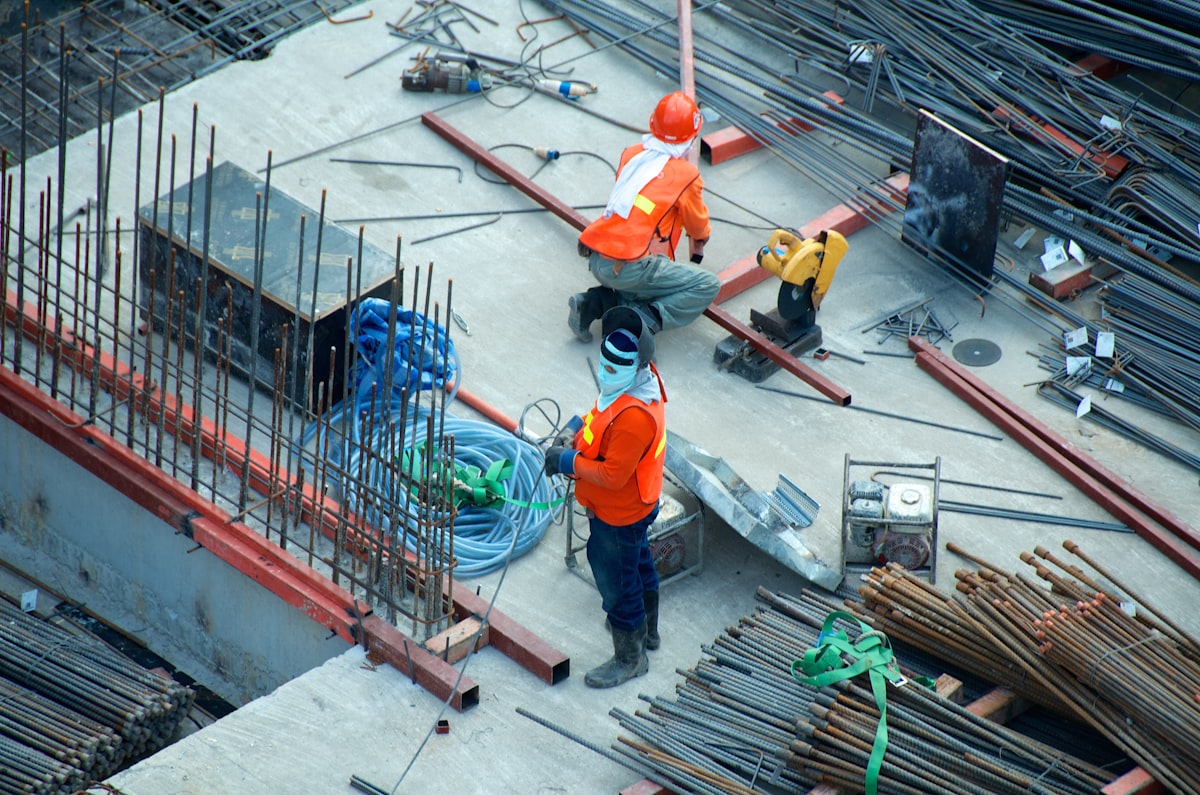 Two workers in high-visibility vests and hard hats among reinforcing bars on a construction deck, seen from above — suggested image — client to supply the final photograph