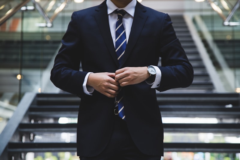 A person in a suit fastening a jacket button, photographed from the shoulders down in an office atrium — suggested image — client to supply the final photograph